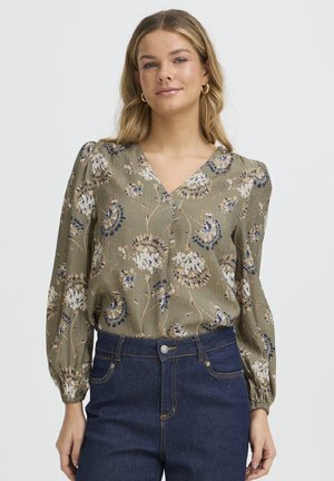 Florale Bluse in Olivgrün mit langen, gepufften Ärmeln, V-Ausschnitt, strukturiertem Stoff und Mustern in Weiß und Marineblau. Kombiniert mit dunklen Jeans aus Denim.