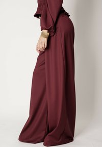 Burgundowe spodnie szerokie z gładkiego materiału, z wysokim stanem i lekko opadającym krojem. Brzeg jest starannie wykończony bez ozdób.