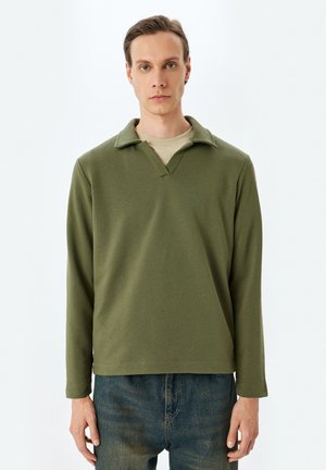 Oliwkowa, długąsleeve koszula z dekoltem w kształcie litery V i kołnierzykiem. Miękka tekstura, luźny krój, w połączeniu z niebieskimi dżinsami.