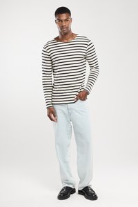 Langärmliges gestreiftes Hemd in Creme und Marineblau, kombiniert mit hellblauen Jeans und schwarzen Schuhen, mit lockerer Passform und strukturiertem Stoff.