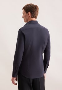 Camicia a maniche lunghe blu navy con una texture liscia, colletto classico e polsini con bottone, caratterizzata da una vestibilità sagomata e un orlo curvo sul retro.