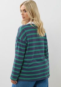 Marinblå långärmad skjorta med gröna horisontella ränder, tillverkad av mjukt tyg. Har en avslappnad passform och sänkta axlar för komfort.