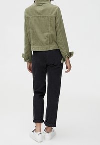 Veste en velours côtelé vert à coupe courte et manches retroussées, associée à un jean foncé et des baskets blanches. La tenue a un look décontracté.