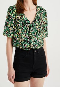 Black floral blouse with short sleeves, featuring green, pink, and white patterns. Paired with high-waisted black denim shorts.