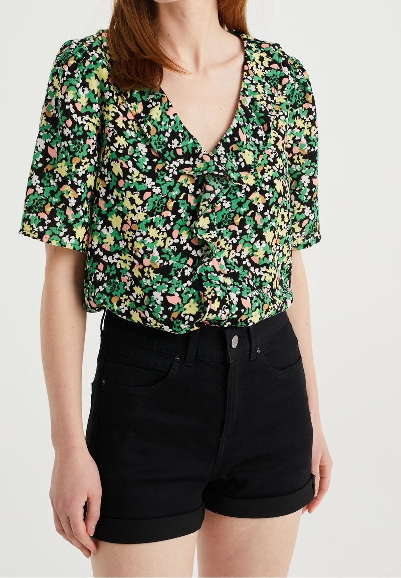 Black floral blouse with short sleeves, featuring green, pink, and white patterns. Paired with high-waisted black denim shorts.