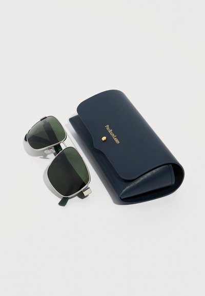 Τετράγωνα γυαλιά ηλίου με ασημένια σκελετό και σκούρους πράσινους φακούς δίπλα σε θήκη από δέρμα σε σκούρο μπλε χρώμα με ανάγλυφο το χρυσό λογότυπο «Polo Ralph Lauren».