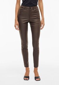 Hnědé skinny džíny s vysokým pasem z lesklého materiálu, s designem pěti kapes, zapínáním na knoflík a úzkým střihem, který se u kotníků zužuje.