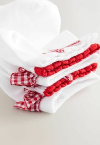 Weiße Socken, gestapelt mit roten Akzenten, ausgestattet mit strukturierten roten Pompons und karierten Stoffdetails entlang der Oberseite. Aus weichem Baumwollmaterial.