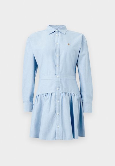 Φόρεμα πουκάμισο μακρυμάνικο σε ανοιχτό μπλε χρώμα με κουμπιά μπροστά, φούστα με ρεβέρ, μυτερό γιακά και μικρό κεντημένο λογότυπο στο στήθος.