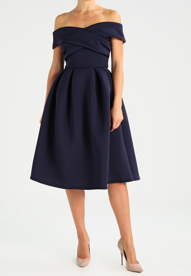 Marinblå klänning med avtagna axlar, en tajt bodice, snodd design och en utsvängd kjol, tillverkad av mjukt tyg. Bärs med hudfärgade klackar.