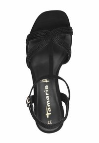 Svart högklackad sandal med flätad remdesign, med en mjuk mockaliknande yta och en smal ankelrem med spänne. Fyrkantig tåform.