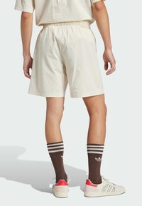 Cream-colored shorts with an elastic waistband, paired with brown striped socks and white sneakers featuring red accents.