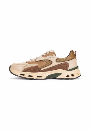 Zapatilla deportiva beige y marrón de caña baja con múltiples texturas, cordones y una suela gruesa con orificios de ventilación sobre un fondo blanco.