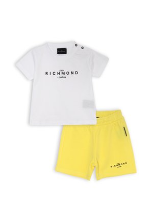 T-shirt bianca in cotone con testo stampato nero e dettagli in bottone, abbinata a pantaloni corti gialli in cotone con vita elastica e stampa del logo.