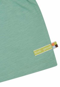 Lichtgroene t-shirt met een gladde textuur, met een label "loud + proud" in het geel en een kleurrijke designrand.