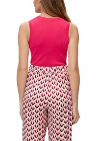 Strakke roze mouwloze top gecombineerd met gemusterde roze en zwarte broek met een elastische tailleband en een bladenpatroon.