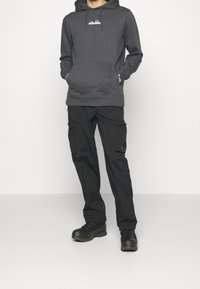 Grå hoodie med känguruficka och dragsko; ihopparat med svarta cargobyxor med sidofickor och orange detaljer; robusta svarta kängor.