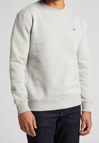 Jasnoszara bluza z okrągłym dekoltem, z prążkowanymi mankietami i dołem. Posiada małe, haftowane logo na klatce piersiowej. Wykonana z miękkiego, teksturowanego materiału.