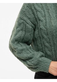 Pull en tricot vert doux et texturé, avec un motif en torsades et des poignets côtelés. Le design comprend des manches longues légèrement bouffantes.