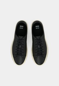 Czarne skórzane sneakersy o gładkiej fakturze, z czarnymi płaskimi sznurowadłami i kremową gumową podeszwą. Na języku znajduje się logo.