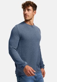 Sininen teksturoitu pyöreäkauluksinen villapaita pitkähihaisilla hihoilla, valmistettu neulotusta materiaalista. Rentoa mitoitusta, yhdistetty vaaleansinisiin farkkuihin.