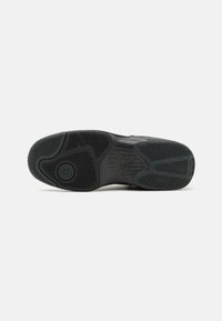 Semelle d'une chaussure de sport noire avec des motifs de bande de roulement texturés et un logo visible au centre, sur un fond neutre.
