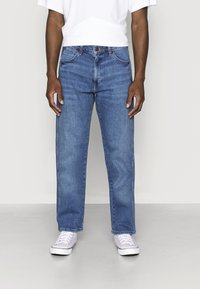 Světle modré džíny z denimu se střihem rovného střihu, designem s pěti kapsami, kontrastním prošitím a zapínáním na zip. Nošeny s bílými teniskami.