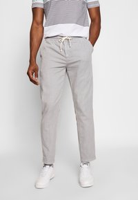 Pantaloni grigi chiari con vita regolabile, vestibilità affusolata e morbida texture, abbinati a sneaker bianche. Camicia a righe indossata sopra.