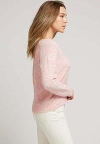 Pull en laine rose avec une texture douce, un col rond et des poignets en côtes. Il présente un ourlet en dentelle et une coupe décontractée.