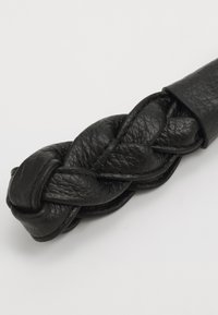 Schwarzes geflochtenes Lederband mit glatter Textur und variierender Dicke, das über eine nahtlose Verarbeitung und eine abgerundete Spitze verfügt.