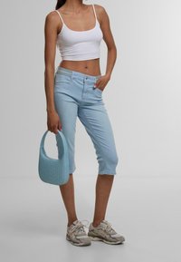 Jeans cropped azzurri chiari con una vestibilità classica, abbinati a un top corto bianco. L'outfit è completato da una borsa a tracolla azzurra chiara con texture e sneakers grigie.