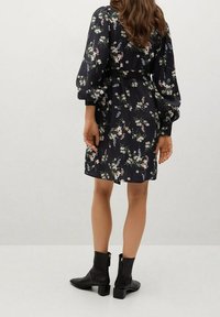 Abito con stampa floreale su sfondo blu scuro, dotato di maniche a palloncino e vita con lace. Indossato con stivali neri alla caviglia.