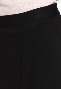 Svarta skräddarsydda byxor med en mjuk textur, med en bred midjeband och subtila veckdetaljer fram.