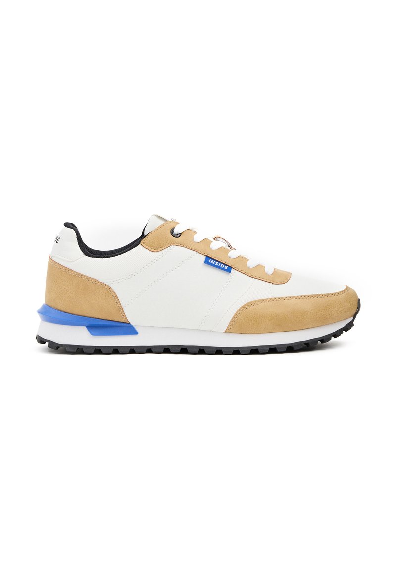 Zapatillas para hombre con un upper sintético blanco, detalles en ante marrón, collar negro, tirador azul en el talón y una suela de goma negra texturizada.