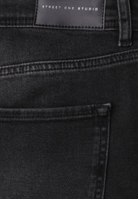 Jean en denim noir avec une finition texturée, doté d'une poche arrière et d'une étiquette en cuir marquée "STREET ONE STUDIO". Design épuré et moderne.