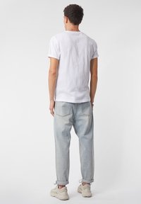 Bílý bavlněný tričko s ohrnutými rukávy, v kombinaci s světle modrými volnými džíny a béžovými teniskami, ukazuje uvolněný styl.