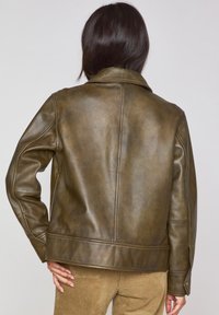 Giacca di pelle marrone con finitura opaca, dotata di colletto a punta, maniche lunghe e dettagli con bottoni sui polsini. Tessuto liscio.