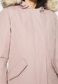 Pink hooded parka with a faux fur trim, featuring a zip and snap closure, side pockets, and a smooth texture with visible stitching.