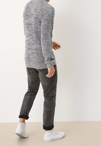 Grauer gestrickter Pullover mit einem strukturierten Muster, kombiniert mit schmal geschnittenen dunklen Jeans und weißen High-Top-Sneakern. Klare Fokussierung auf die Details des Outfits.