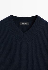 Maglione lavorato a maglia blu navy con scollatura a V, caratterizzato da una texture a coste e un'etichetta con la scritta "Massimo Dutti" all'interno della scollatura.