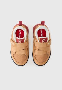 Braune Sneakers mit Mesh-Obermaterial, doppelten Klettverschlüssen, gepolstertem Schaft und roten Akzenten. Schwarze Sohlen mit strukturiertem Profil für besseren Halt.