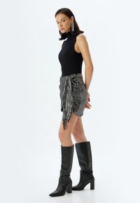 Top sin mangas de canalé negro, falda de lentejuelas en blanco y negro con un lazo, y botas de tacón negro hasta la rodilla. Diseño ajustado y texturizado.