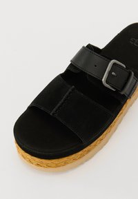 Sorte semsket plattform sandal med to justerbare stropper, en metallspenne og en vevd jute-midtsole. Teksturert fotseng for komfort.