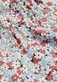 Tissu floral avec de petites fleurs blanches, bleues et rouges sur un fond vert clair ; matériau texturé et côtelé avec une finition douce.