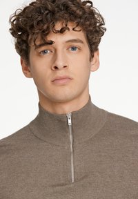 Brun zip-up tröja med en ribbad hög krage och en slät textur. Har en silverdragkedja och en smal passform.