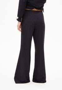 Marineblaue, gestreifte, ausgestellte Hose mit glatter Stoffoberfläche und mittelhohem Bund, die ein dezentes Rückenschlitzdetail aufweist.