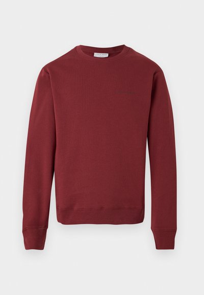 Maroon long-sleeve crewneck sweatshirt with ribbed cuffs and hem, minimal logo text on the upper left chest, set against a white background.