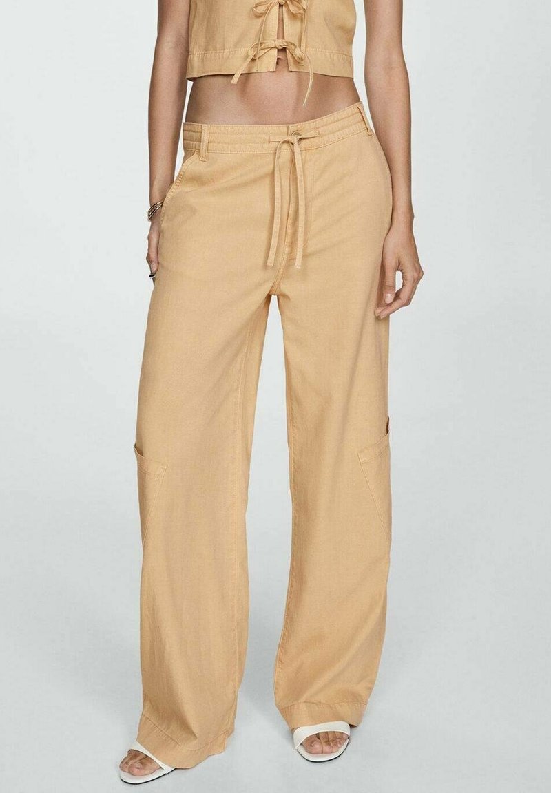 Béžové, široké kalhoty s šňůrkovým pasem a bočními kapsami. Vyrobeny z měkké, lehké tkaniny s uvolněným střihem a čistými liniemi.