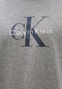 Γκρίζο βαμβακερό T-shirt με μεγάλο μαύρο λογότυπο "CK" και κείμενο "CalvinKlein" σε λευκό, στρογγυλή λαιμόκοψη και κοντά μανίκια.
