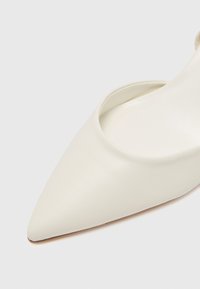 Pointed-toe white leather shoe with a sleek design and open sides, featuring a smooth texture and a slim heel.